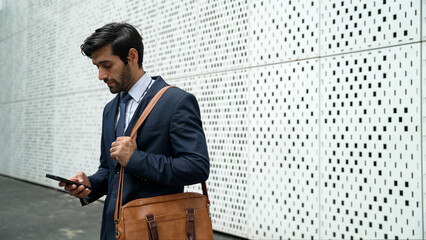 Smart manager looking at mobile phone and walking at street while wearing suit. Skilled investor...