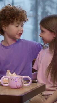 Children sitting together at a table in a restaurant. Stock footage. Brother with red curly hair putting ihs arm around the shoulders of her cute sister.