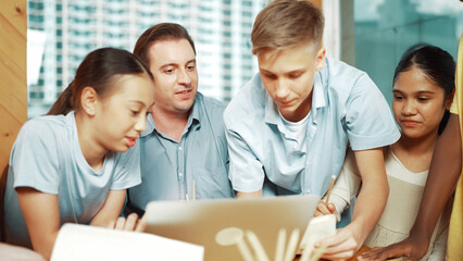 Caucasian teacher giving advise to young student while boy lecture comment. Professional instructor write comment surrounded by multicultural children at table with laptop and paper. Edification.