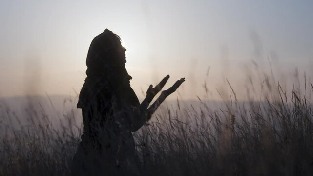 Muslim woman with a veil sitting on ground praying outdoors