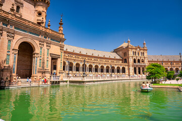 Naklejka premium Sevilla, Spain - April 10, 2023: Several boats with people rowing at leisure on the lake of Plaza de Espana with buildings in the background