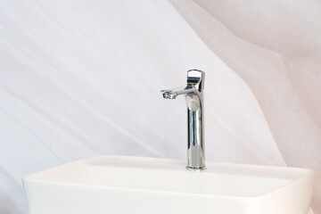 A chrome faucet is mounted on a white sink in the interior of a light beige bathroom