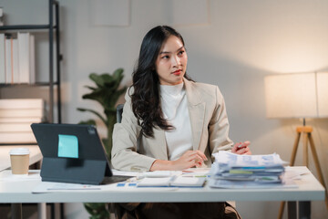 Focused Determination: A contemplative businesswoman sits at her desk, immersed in her work, surrounded by paperwork and a tablet. She embodies concentration and dedication, highlighting the importanc