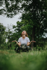 A young woman engages in mindfulness meditation outdoors, seated on grass in a tranquil park...
