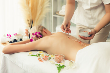 Obraz na płótnie Canvas Woman customer having exfoliation treatment in luxury spa salon with warmth candle light ambient. Salt scrub beauty treatment in health spa body scrub. Quiescent
