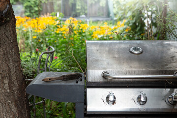 Steel gas burner grill with a garden full of yellow flowers defocused in the background
