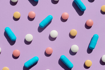 Pattern of several pills and tablets blue, pink, yellow and white colors on purple background. Creative tablets concept