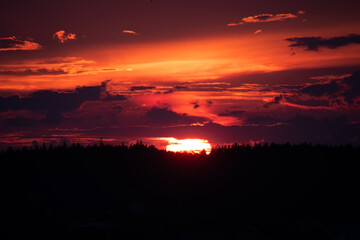 The breathtaking scarlet sunset scene is filled with vibrant hues that beautifully and dramatically color the darkened horizon and silhouettes of the countryside