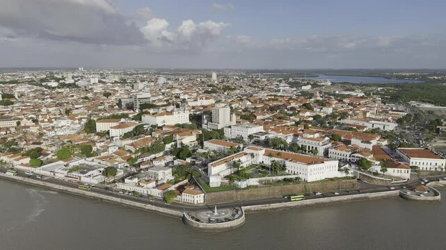 Drone flies to the right high over Rio Anil next to historic center at high tide, passing in front of iconic landmarks in Sao Luis, Maranh&atilde;o, Brazil