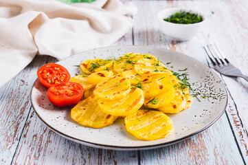 Appetizing grilled potatoes with tomatoes and dill on a plate on the table
