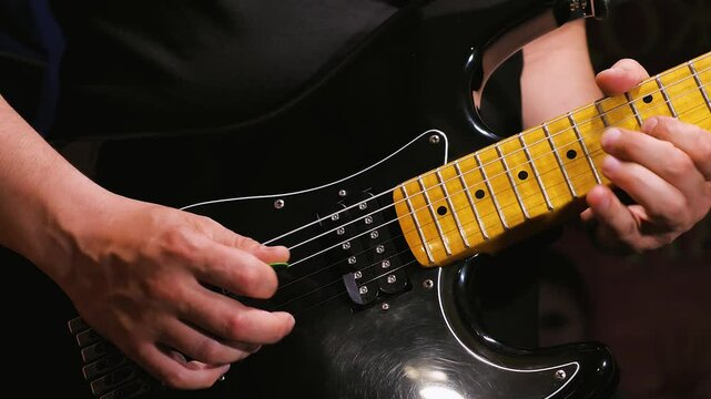 A man plays a solo on a black electric guitar with a yellow fingerboard. Slow motion. Guitarist honing his guitar playing skills