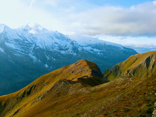 Fototapeta premium Mountainous landscape with verdant mountain slope in front of bare snow-capped mountain peaks in autumn in Austria.