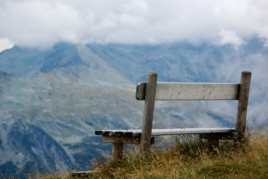 Close-up of a wooden bench with a view of an amazing mountain landscape on a hazy day with gray clouds and fog over the peaks in autumn in Austria.