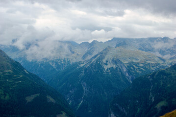 View of an amazing mountain landscape on a hazy day with gray clouds and fog over the peaks in autumn in Austria.