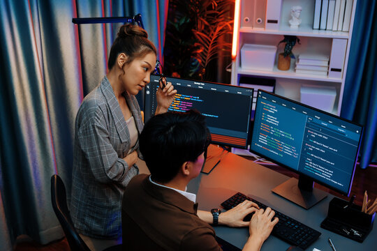 IT developers discussing with point to intelligent website development coder system running data online on pc of two screens with information technology at neon light room at modern office. Infobahn.