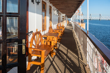 the promenade deck of a wheeled antique steamship of the early 20th century against the background of a river and a modern bridge in the distance