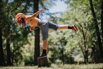 Red-haired woman performs a balancing pose on a tree stump in nature, embodying poise and control.