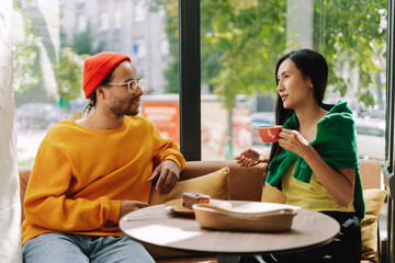 Attractive, smiling couple, Asian woman and Latin man enjoying coffee and conversation in cafe