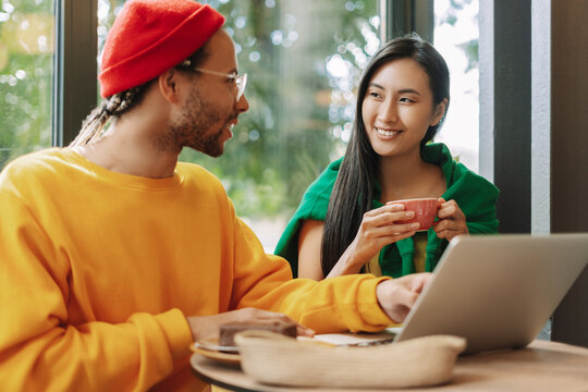 Young international couple working on laptop and having coffee break in cafe