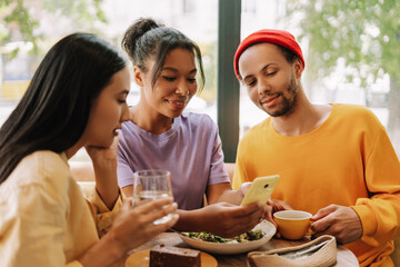 Three diverse, multinational friends using mobile phone sharing social media content