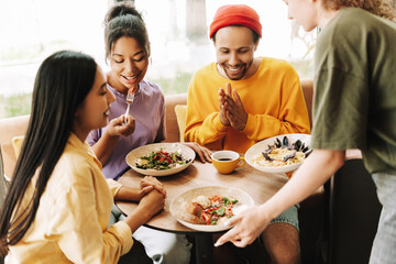 Waitress bringing food to diverse group of friends eating in restaurant