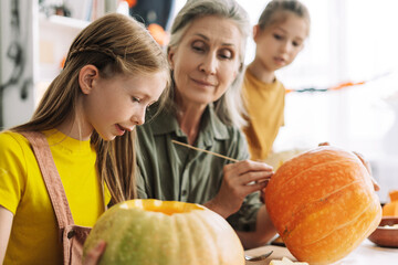 Fototapeta premium Grandmother helping little girls carving pumpkins for halloween celebration