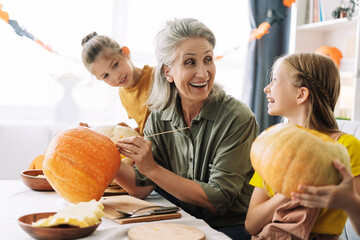 Grandmother and two little cute granddaughter carving pumpkins together for halloween celebration