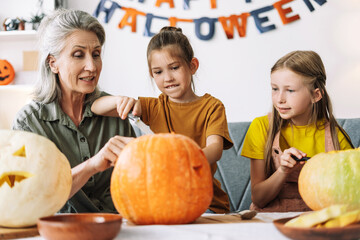 Attractive grandmother and granddaughters carving pumpkins for halloween celebration