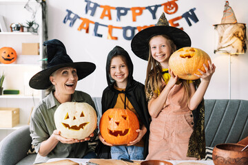 Fototapeta premium Senior woman and little, attractive girls costumes celebrating halloween posing with carved pumpkins