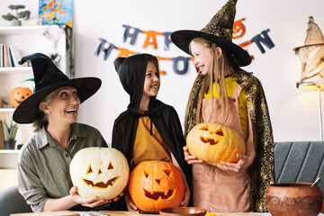 Mature woman and little girls wearing witch hats holding carved pumpkins celebrating halloween