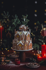Elegant luxury Christmas table setting for family home party with homemade big gingerbread house, holiday celebration. Red tablecloth, candles, chandelier. Romantic candlelit dinner