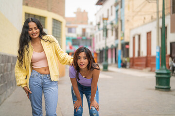 Two young women walking down a city street, one bending over with tired legs