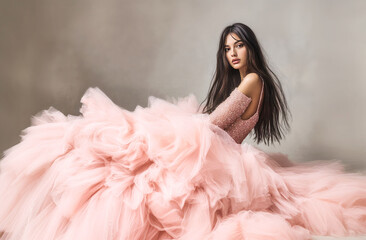 Elegant woman in a luxurious pink tulle gown sitting gracefully, showcasing glamour, fashion, and sophistication with a dreamy expression