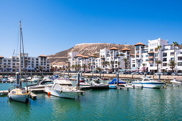 Obraz premium Seaside view of Agadir Marina in Morocco. Popular tourist area with luxury apartments, boats in harbor, shops and restaurants. Moroccan seaside resort on shore of Atlantic ocean in Africa