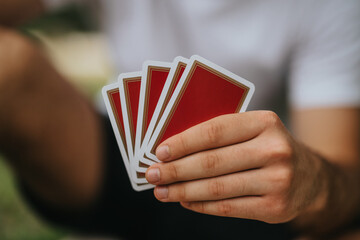 A close-up image of a person holding a fan of red playing cards, suggesting leisure activity or a...