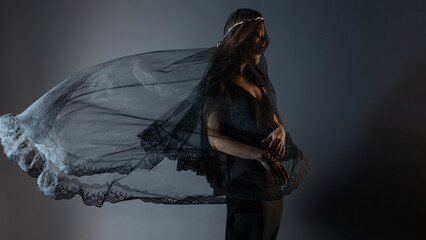 A mysterious woman in black, folds of a veil hide her face, portrait on a dark background