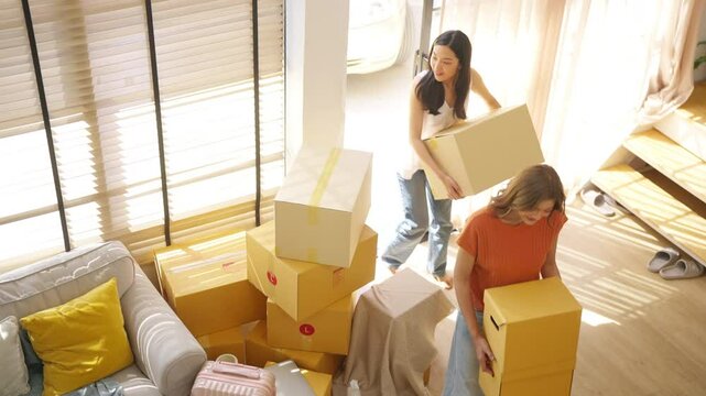 Happy Asian woman lesbian couple carrying cardboard boxes walking into new house. People family relocation moving new home. Marriage equality, Real estate financial, mortgage, home insurance concept.
