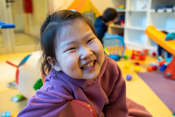 young girl is smiling and sitting on the floor in a room full of toys