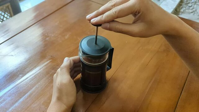 Close up a hands pushing down on the filter plunger of a cafeti&egrave;re or French press, To make a coffee menu in the home, prepare to make caffeine drinks, 4K.