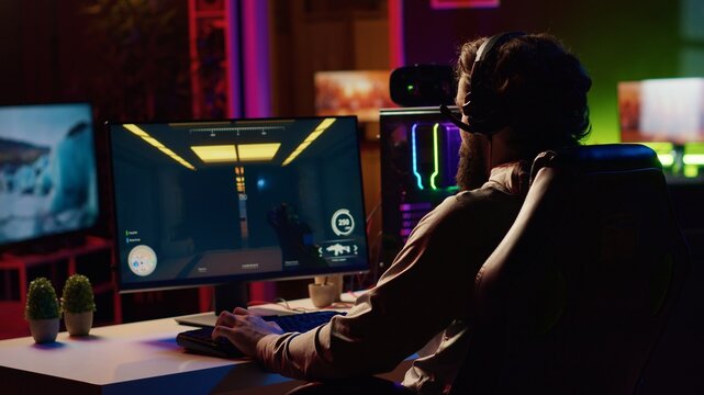 Man coming to gaming station, excited to finally relax by playing SF videogame on PC at computer desk late at night. Gamer starting game, battling foes in online multiplayer futuristic shooter