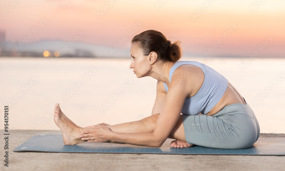 Wall mural Portrait of young sporty woman making stretching legs and yoga pose on beach at morning outdoors