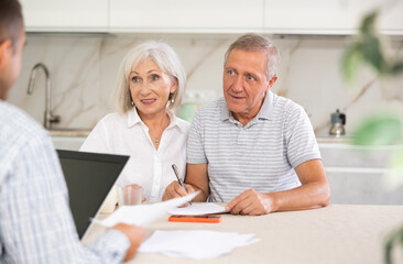 Young salesman explaining terms of deal to elderly couple sitting in kitchen. Health insurance concept