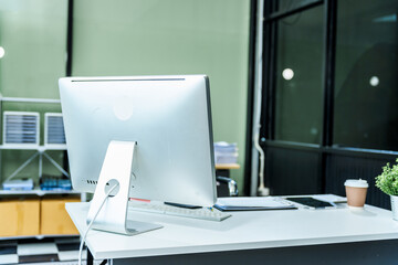 A sleek modern desk with a computer and laptop sits empty in a glass office, reflects a contemporary style with no people present, emphasizing a clean, professional environment.