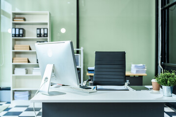 A sleek modern desk with a computer and laptop sits empty in a glass office, reflects a contemporary style with no people present, emphasizing a clean, professional environment.