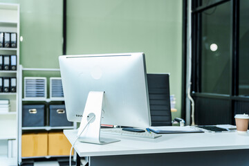 A sleek modern desk with a computer and laptop sits empty in a glass office, reflects a contemporary style with no people present, emphasizing a clean, professional environment.