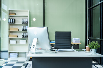 A sleek modern desk with a computer and laptop sits empty in a glass office, reflects a contemporary style with no people present, emphasizing a clean, professional environment.