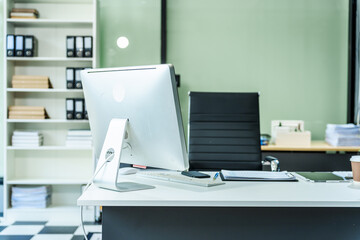 A sleek modern desk with a computer and laptop sits empty in a glass office, reflects a contemporary style with no people present, emphasizing a clean, professional environment.