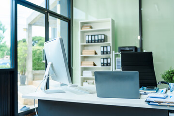 A sleek modern desk with a computer and laptop sits empty in a glass office, reflects a contemporary style with no people present, emphasizing a clean, professional environment.