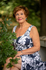 A woman in a floral dress poses gracefully among greener