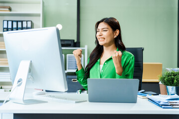 successful and happy young Asian businesswoman in a formal suit works at her desk in a modern glass office. consults on business strategies LGBTQ inclusivity, managing multiple projects efficiently.